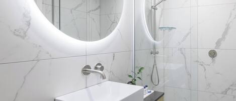 Un baño moderno con lavamanos de mármol blanco, ducha con cerramiento de vidrio y un espejo grande.