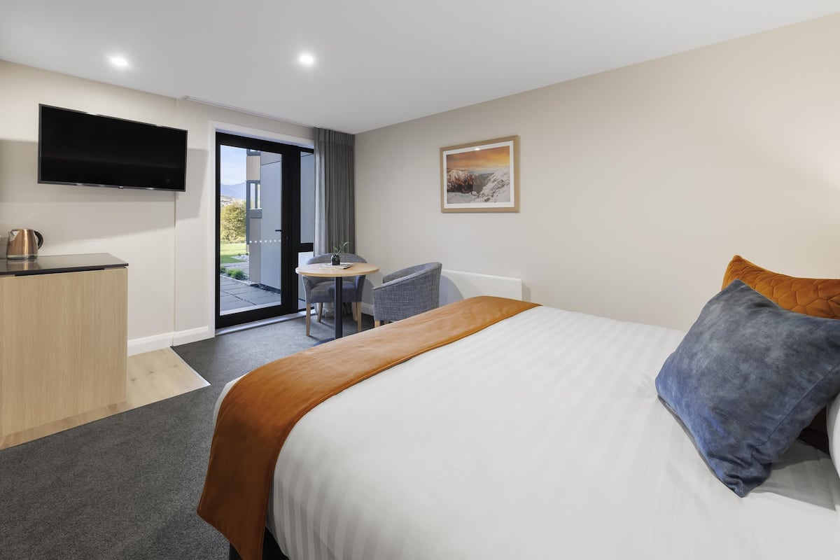 Una habitación de hotel moderna con una cama grande, un escritorio, una silla, un televisor de pantalla plana y una puerta que da a un balcón.