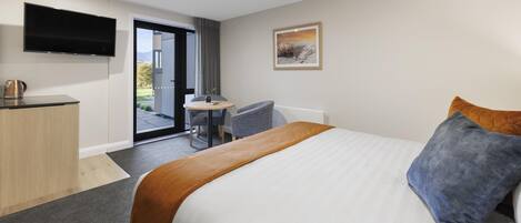 A modern hotel room with a large bed, a desk, a chair, a flat-screen TV, and a door leading to a balcony.