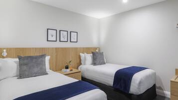 A hotel room with two beds, a wooden headboard, a nightstand with a lamp, and framed artwork on the wall.