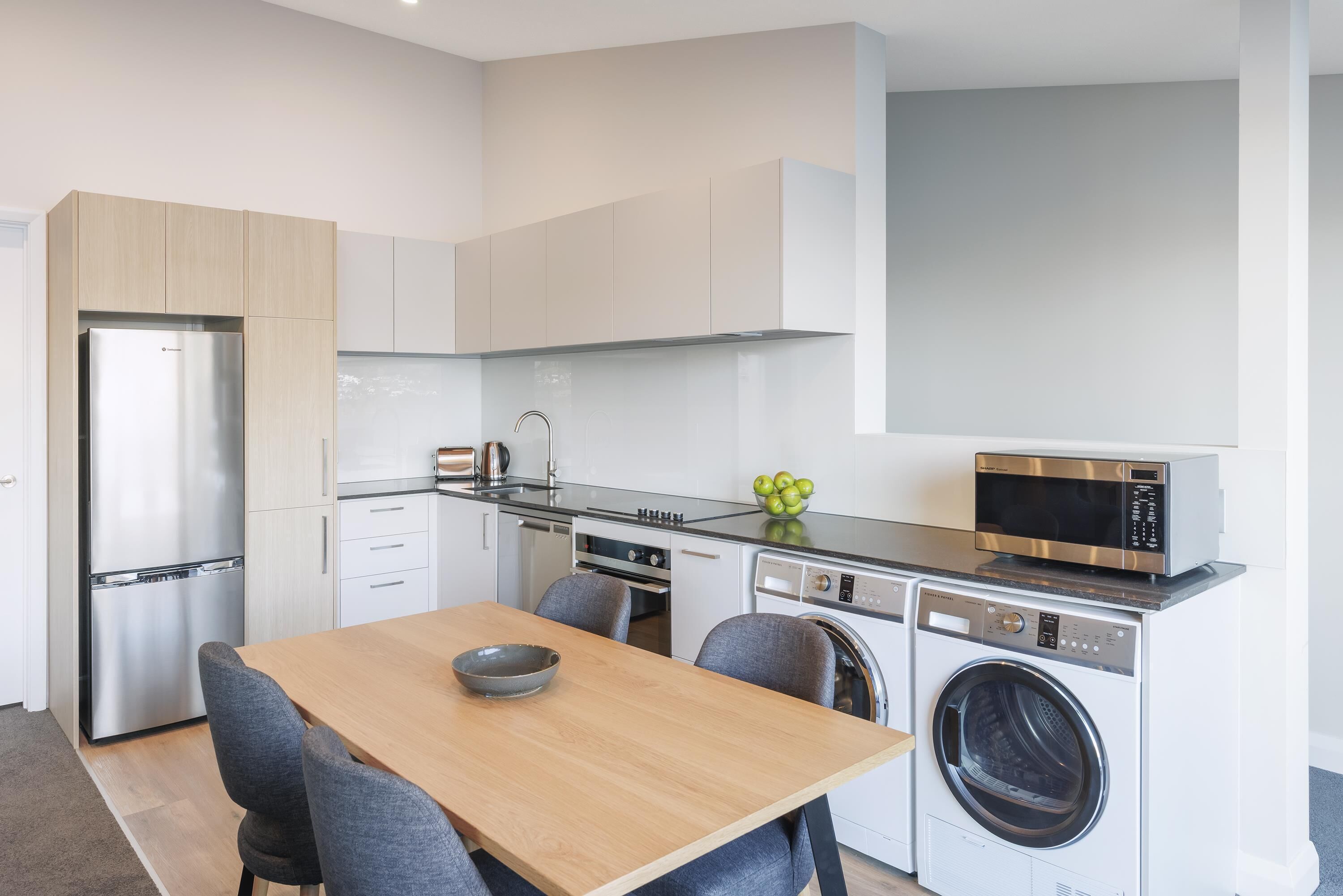 A compact kitchen with a stainless steel refrigerator, a microwave, a dishwasher, and a washing machine.