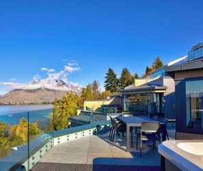 Une terrasse extérieure moderne, dotée d’une balustrade en verre, qui offre une vue sur un lac et des montagnes.