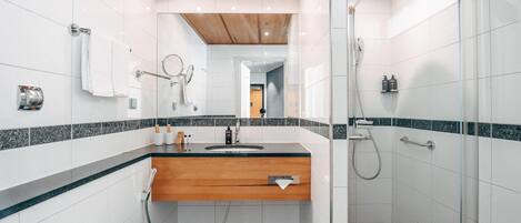 Un baño moderno con techo de madera, baldosas blancas, un lavamanos con encimera de madera, cabina de ducha de vidrio y un inodoro a la vista.