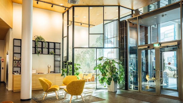 Una moderna zona de recepción con puerta de cristal, sillas amarillas y plantas de interior.
