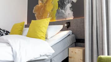 Un letto rifatto con cuscini bianchi e gialli, una testiera grigia e un comodino di legno.