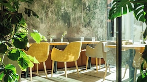 Un comedor moderno con sillas y mesas de madera, rodeado de grandes plantas verdes.