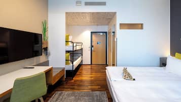 A modern hotel room with a bed, a desk with a chair, a television, and a small plant.