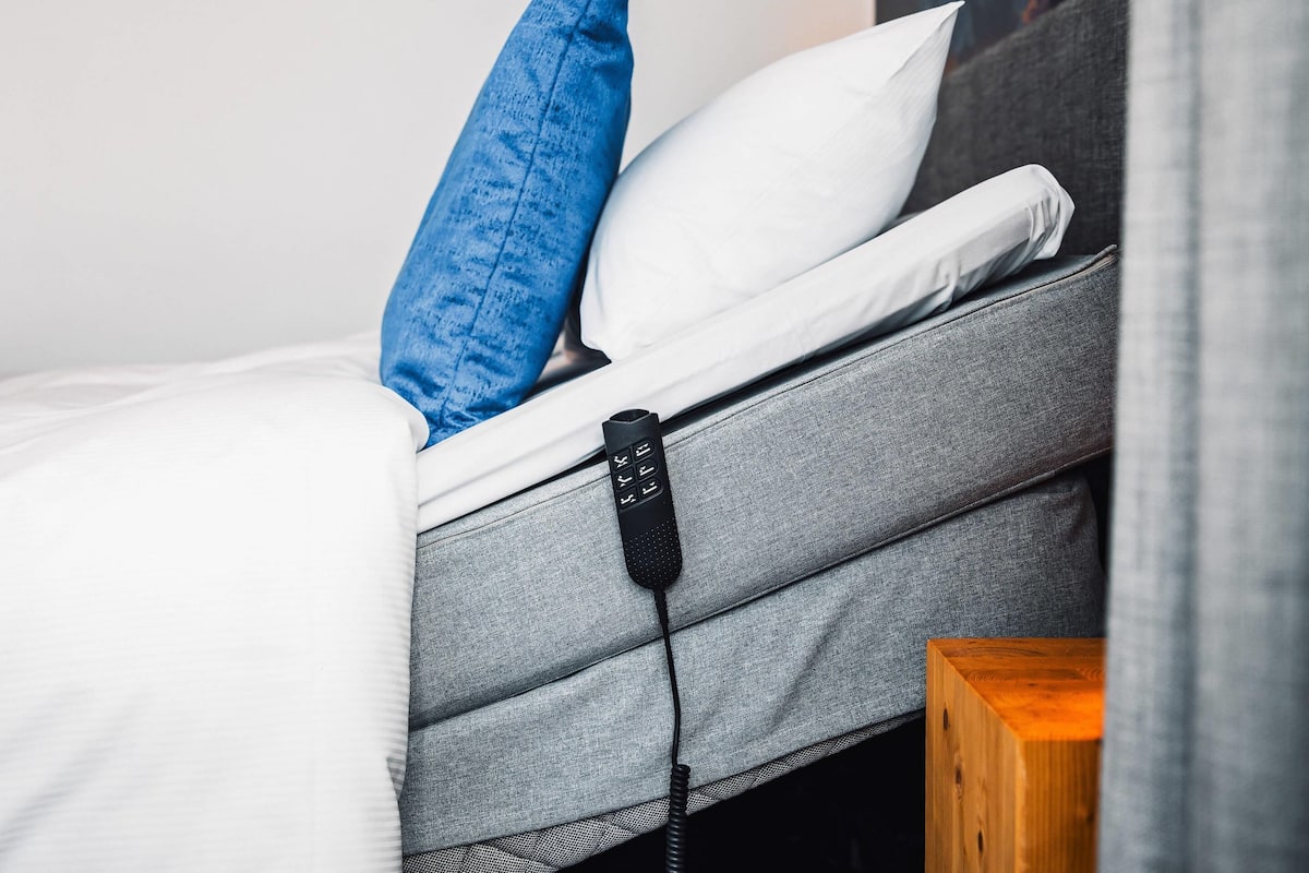 A bed with a grey headboard, white bedding, and a blue pillow.