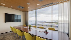 Un salón de conferencias con una gran mesa, sillas amarillas, un televisor de pantalla plana y vistas de la ciudad a través de amplias ventanas.