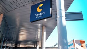 Una entrada de hotel moderna con un letrero de 'Comfort Hotel', ventanas grandes y estructura metálica.