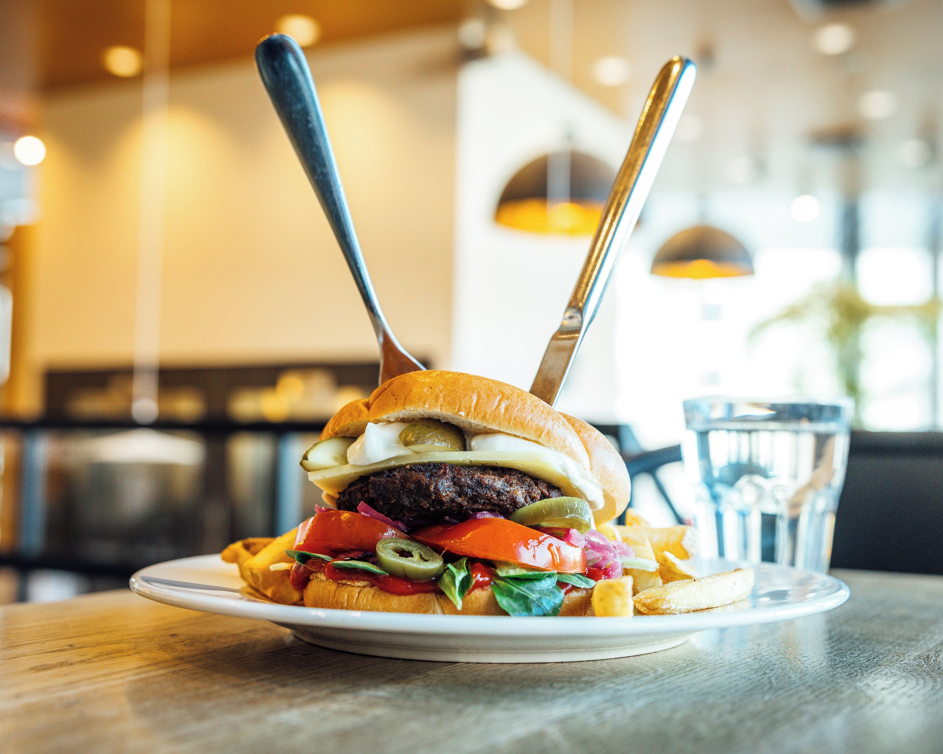 A burger with pickles, cheese, and lettuce on a plate, accompanied by fries and a glass of water.