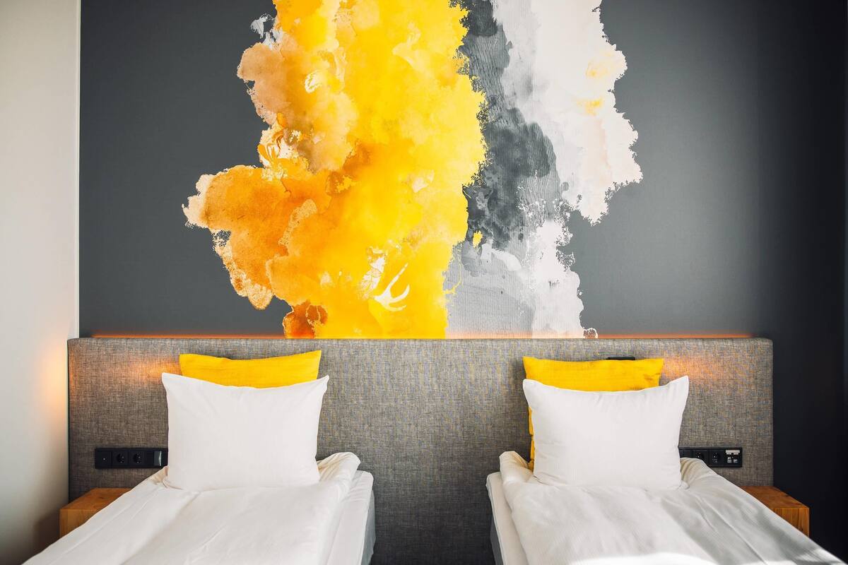 A hotel room with two beds, a grey headboard, and a large abstract painting on the wall.