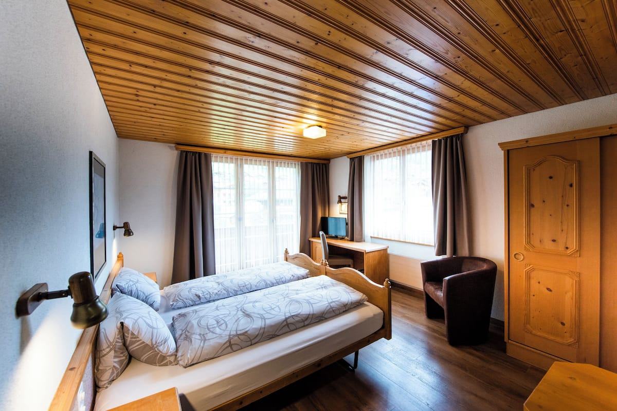 Una camera da letto con soffitto in legno, un letto con copriletto decorato, una scrivania con sedia e un armadio.