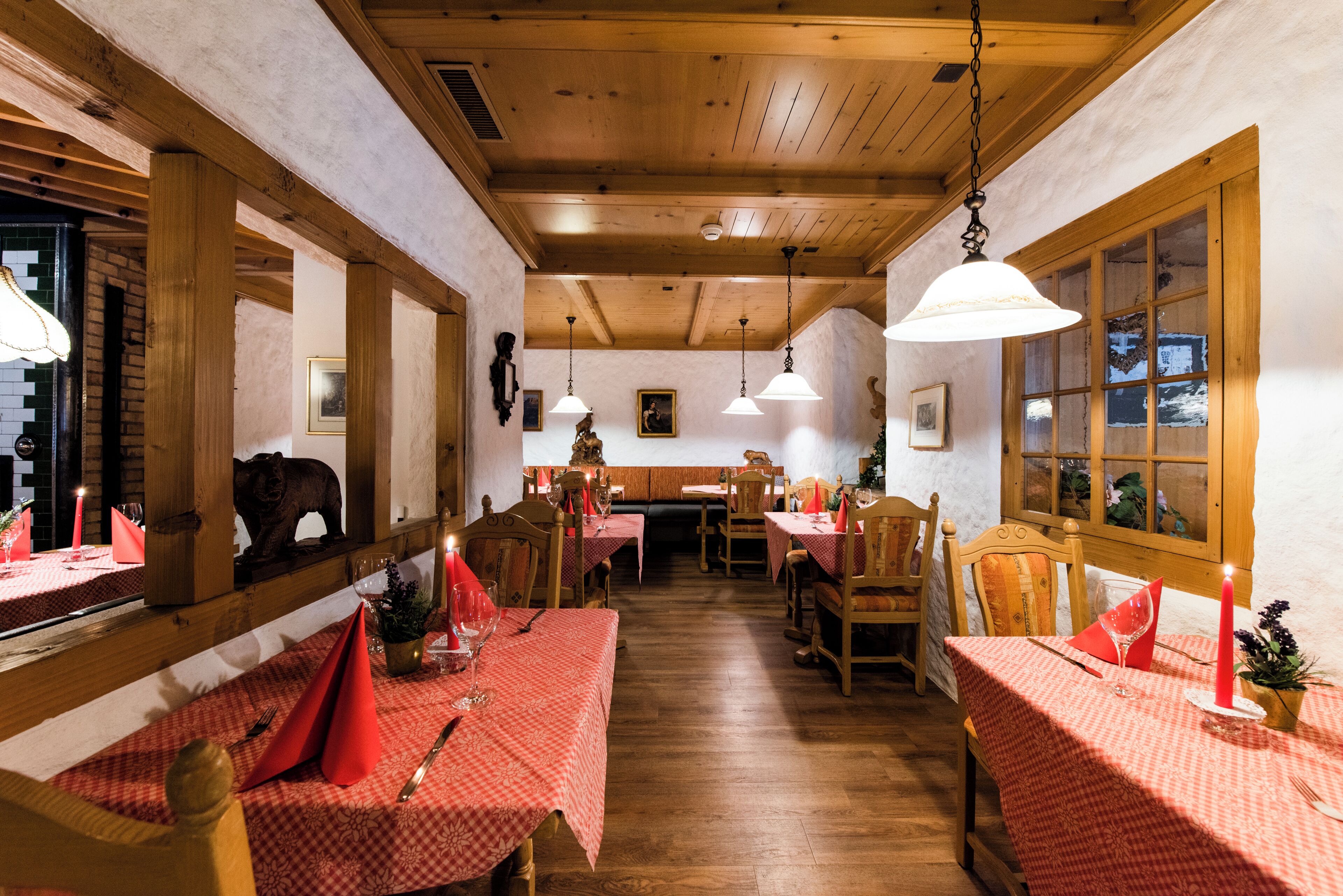 Un restaurant aux poutres apparentes et aux nappes à carreaux rouges. Les tables sont décorées de bougies et de verres à vin.