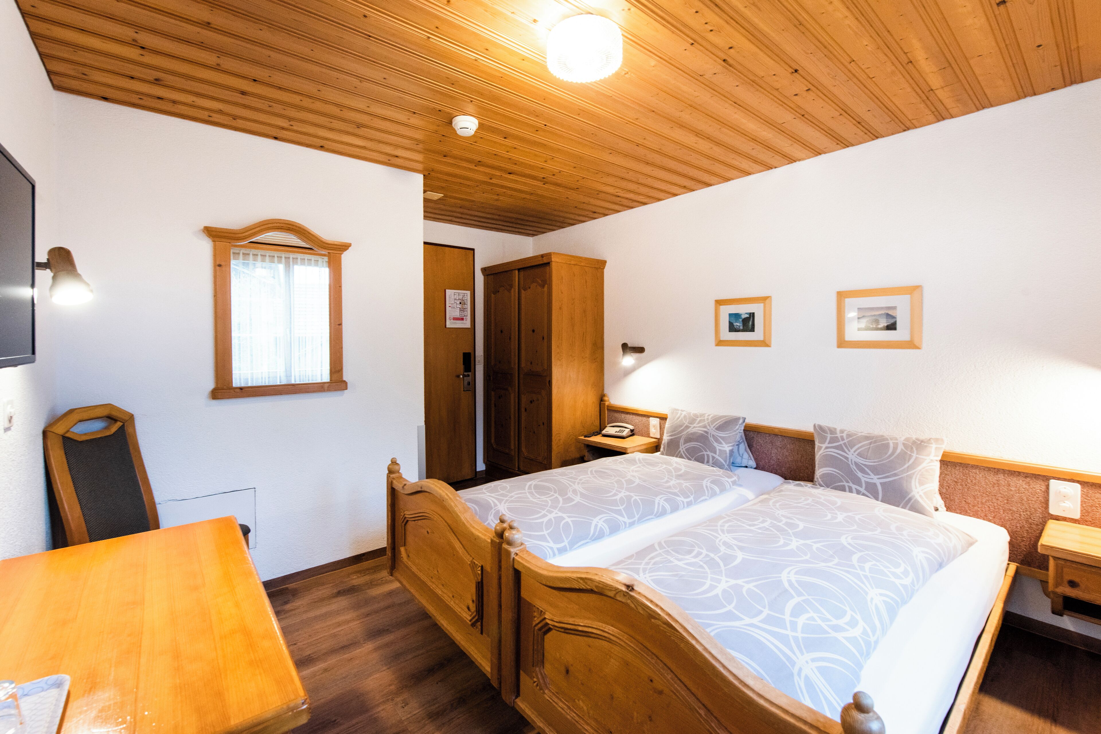 Une chambre aux murs lambrissés, avec un lit, une table en bois et un miroir.