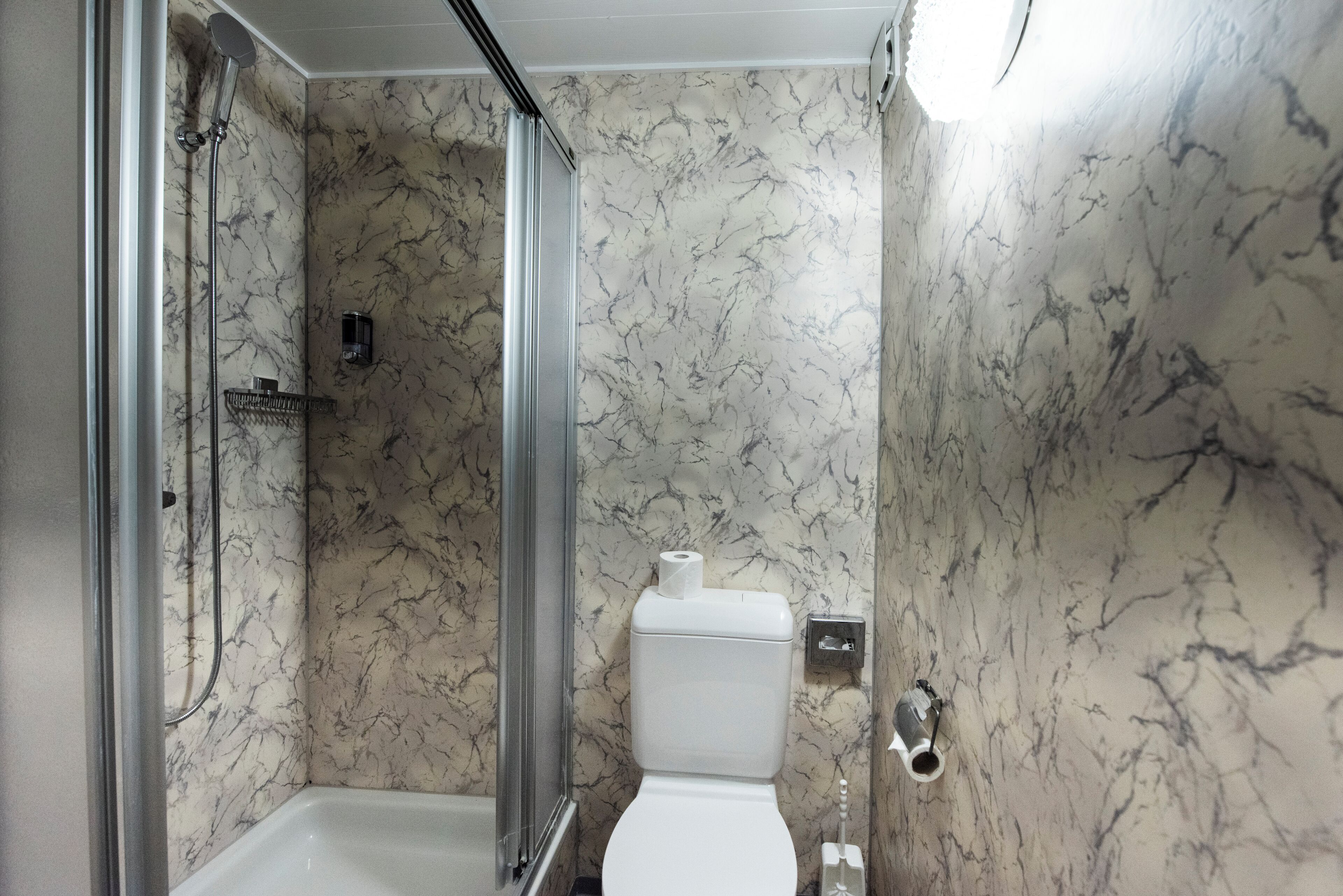 Une salle de bain avec douche, toilettes et murs en marbre.