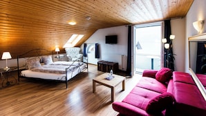 Un dormitorio con una cama, un sofá rojo, una mesa de centro de madera, una mesita de noche con una lámpara, una silla y un televisor en la pared.