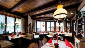 Un comedor rústico con mesas y bancos de madera, ventanas amplias y lámparas colgantes.