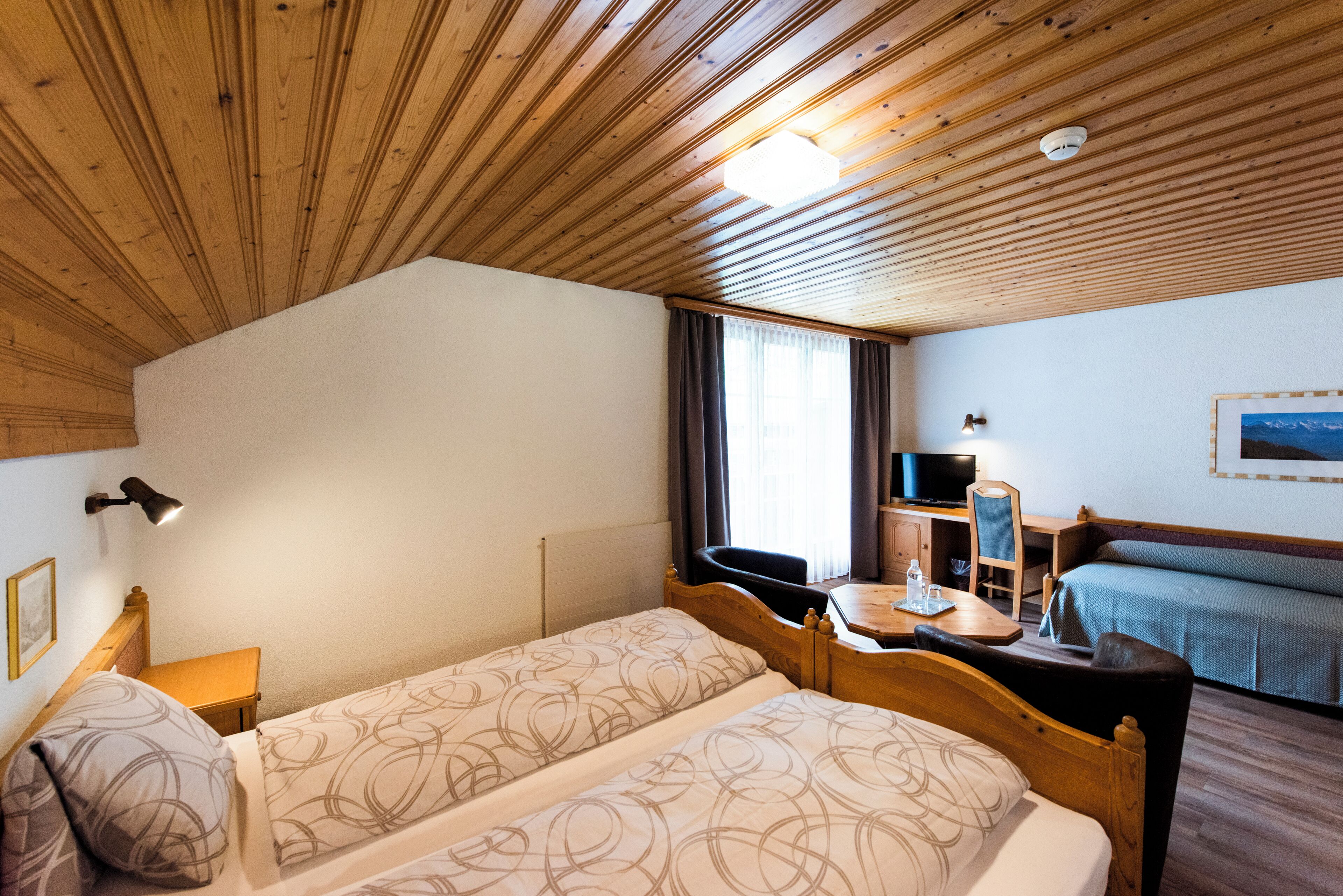 Habitación de hotel con dos camas, un escritorio, televisor y ventana con cortinas.