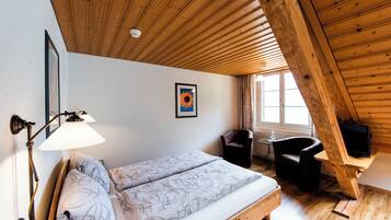 Un dormitorio con techo de madera, una cama con ropa de cama estampada, un escritorio con televisor y una silla.