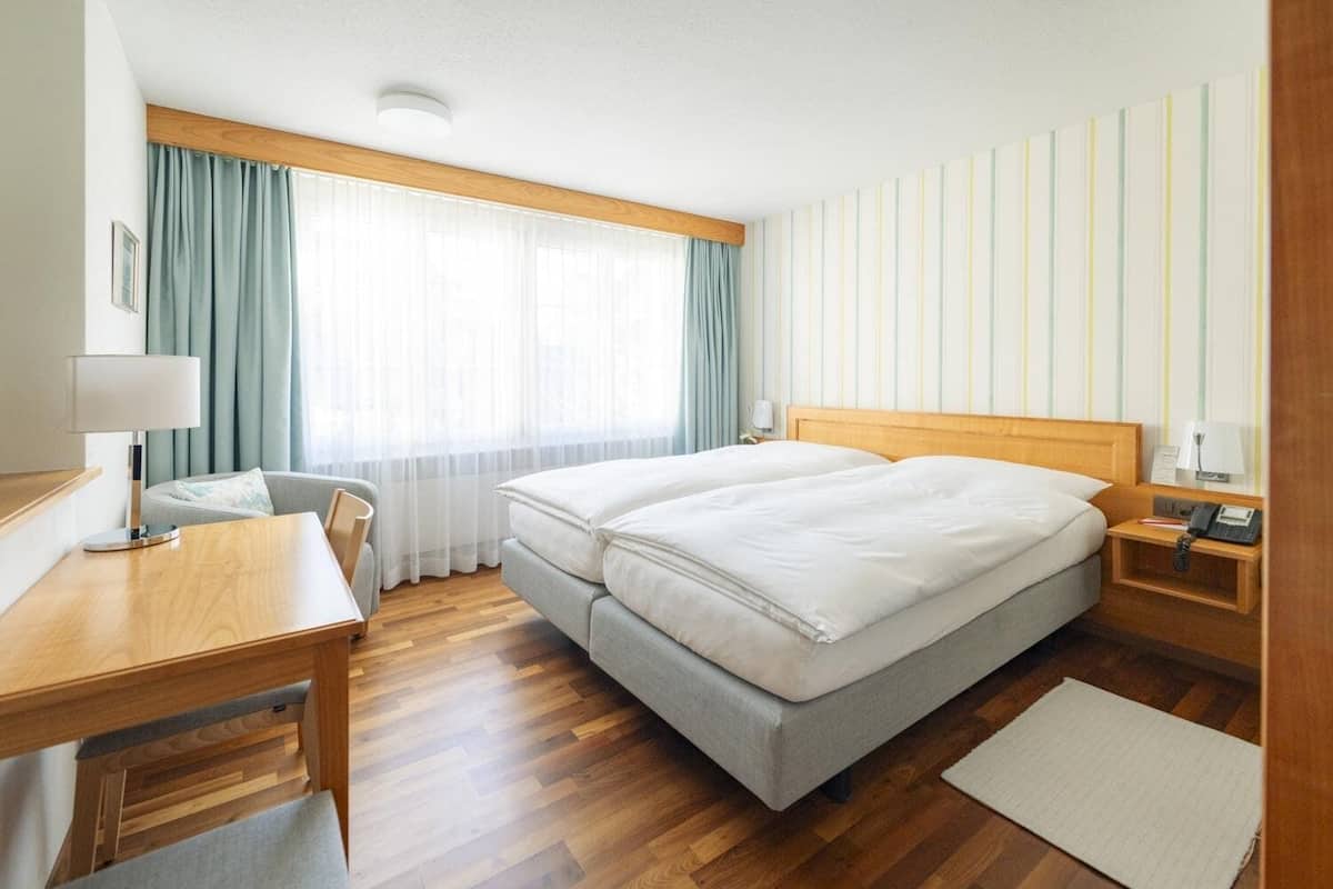 Ein Hotelzimmer mit Holzboden, einem Doppelbett, einem Schreibtisch mit Lampe, einem Stuhl und einem Nachttisch mit Telefon.
