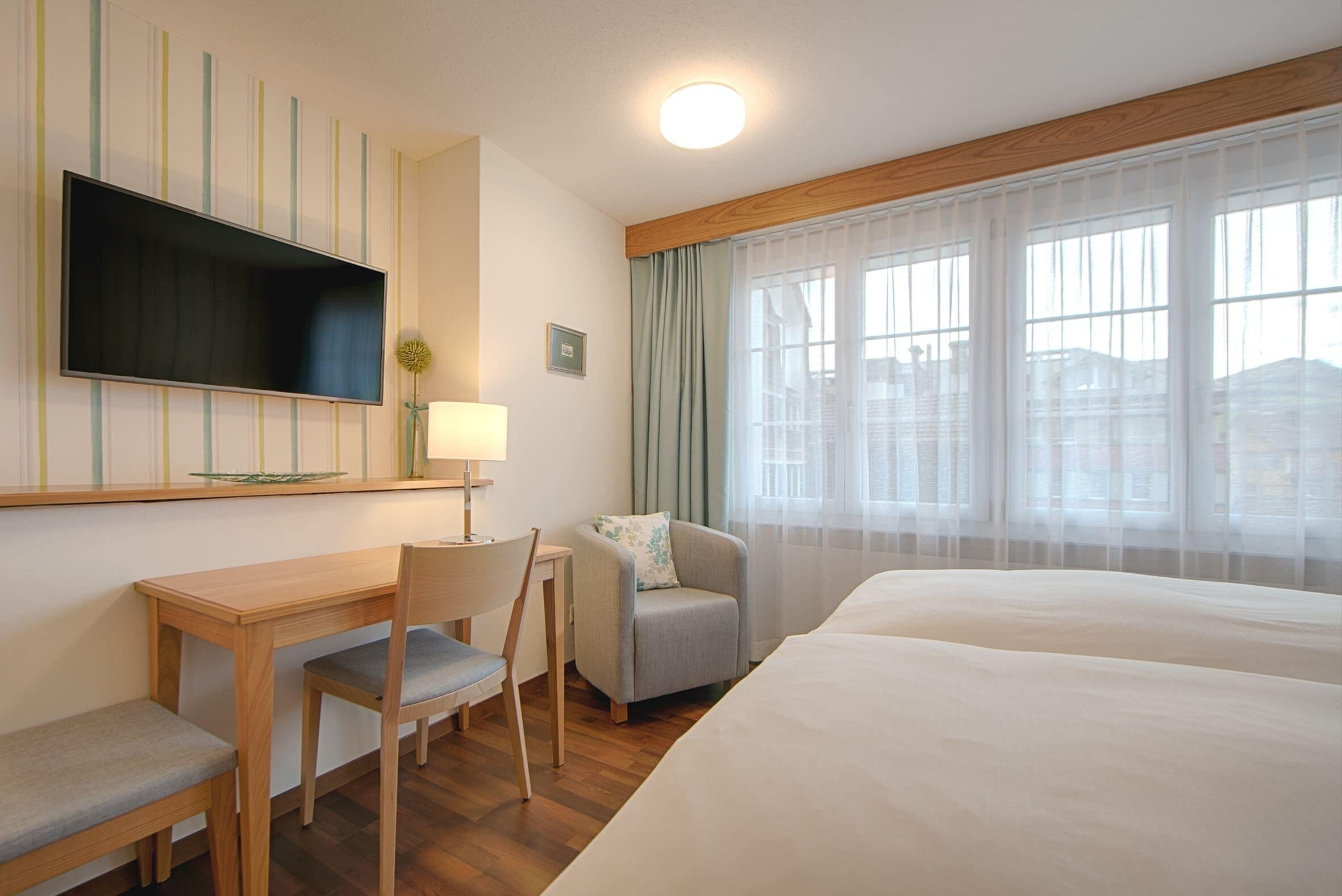 Een hotelkamer met een bed, een bureau, een stoel, een televisie en een raam met gordijnen.