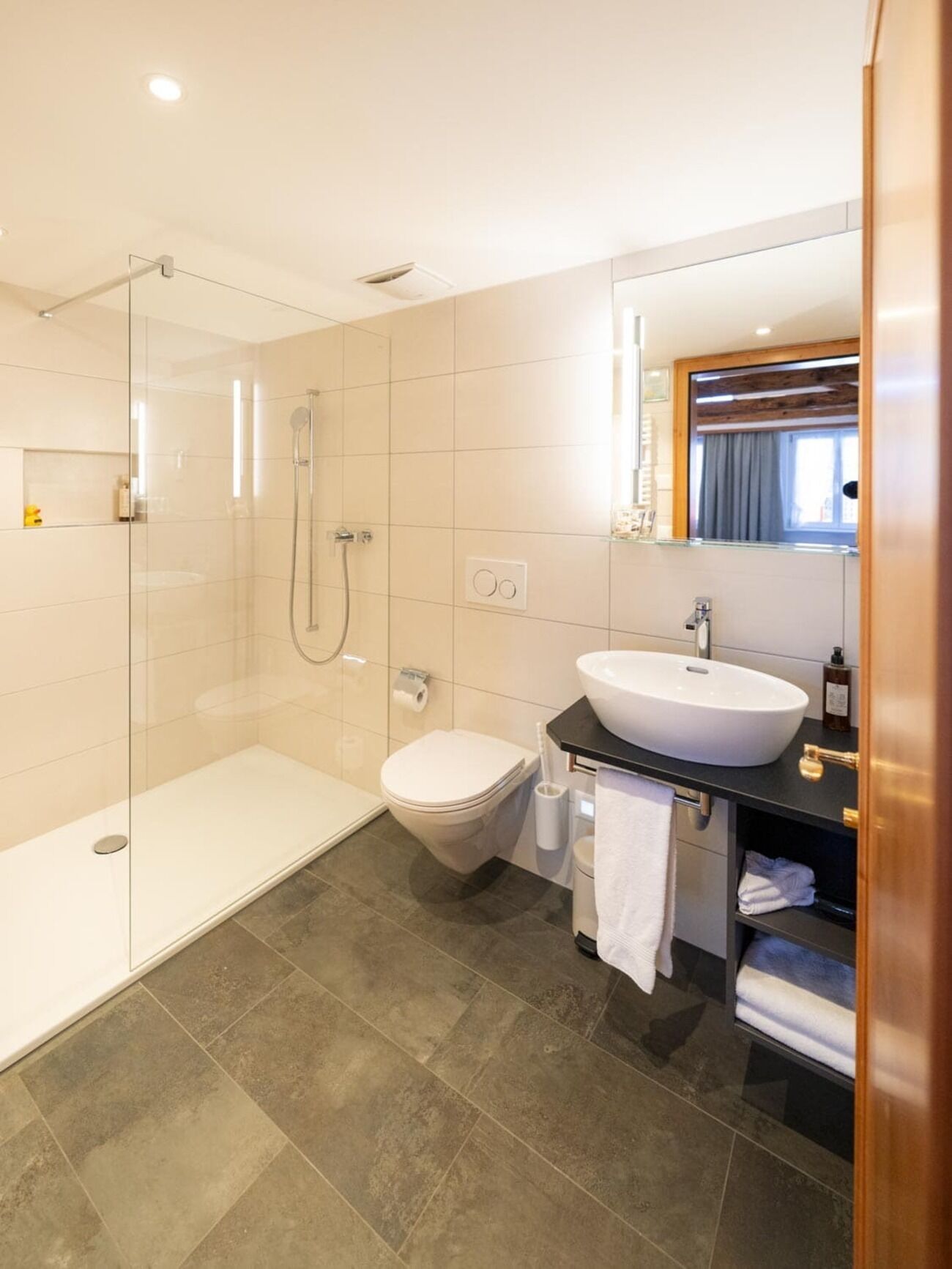A modern bathroom with a glass shower enclosure, a white toilet, and a black sink with a mirror above.