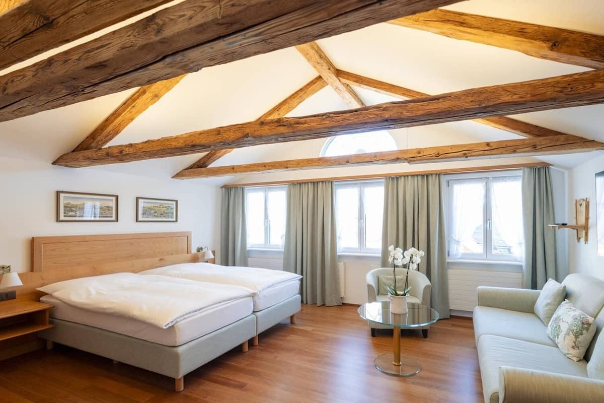 Ein Schlafzimmer mit Holzbalkendecke, einem Bett, einem Sofa, einem Sessel und einem Fenster mit Vorhängen.