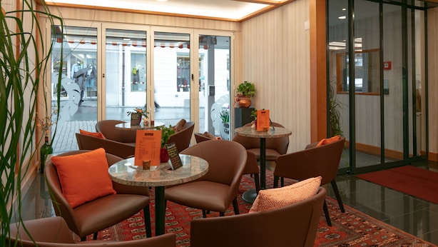 A lobby with round tables and chairs, a patterned rug, and potted plants. - Hotel Löwen (Appenzell)