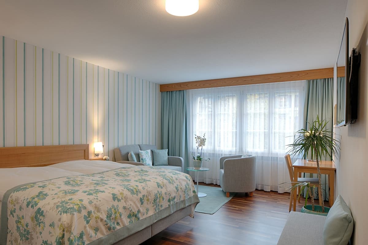 Ein Hotelzimmer mit einem großen Bett, einer Couch, einem Esstisch und einer Zimmerpflanze.