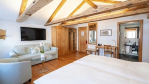 A modern bedroom with exposed wooden beams, a large bed, a sofa, a small table with a vase, and a bathroom visible through an open door. - Hotel Löwen (Appenzell)