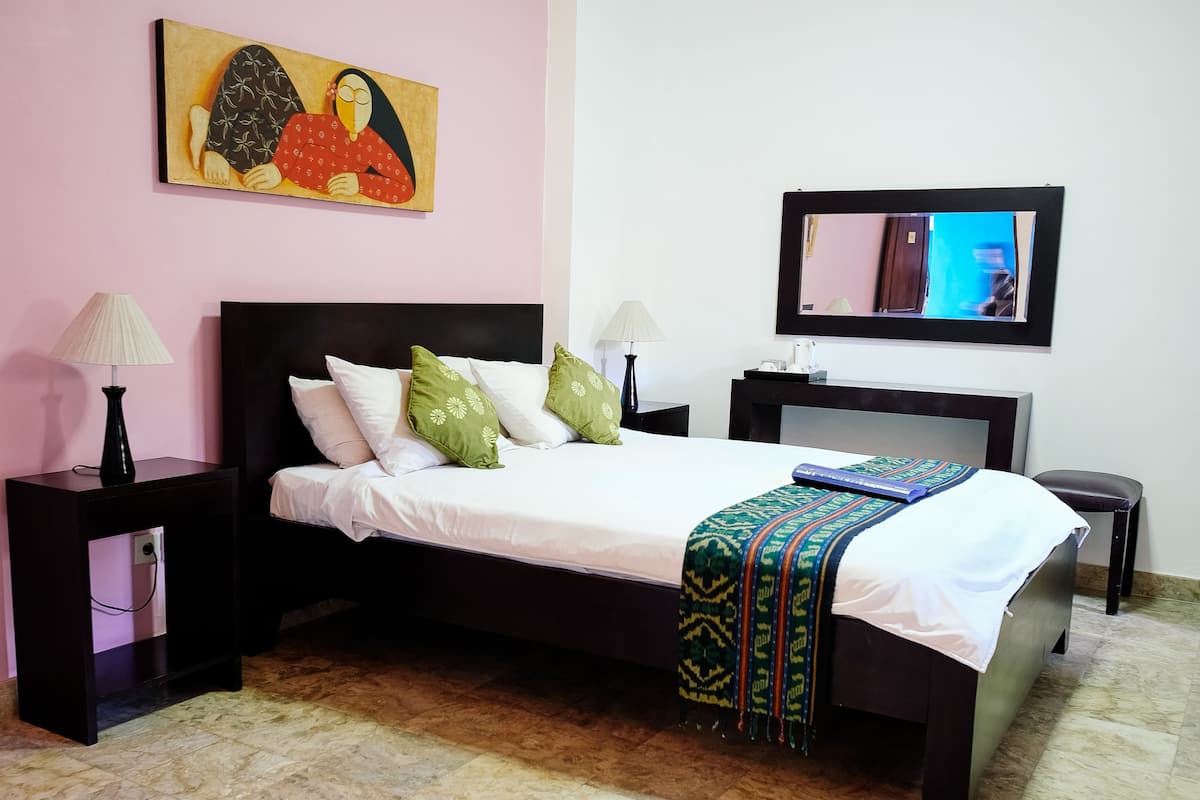A bedroom with a bed, a nightstand, a lamp, a television, and a painting on the wall.