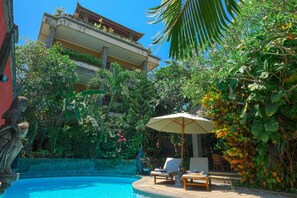 Area piscina con lettini e ombrellone, immersa nel verde e con un edificio sullo sfondo.