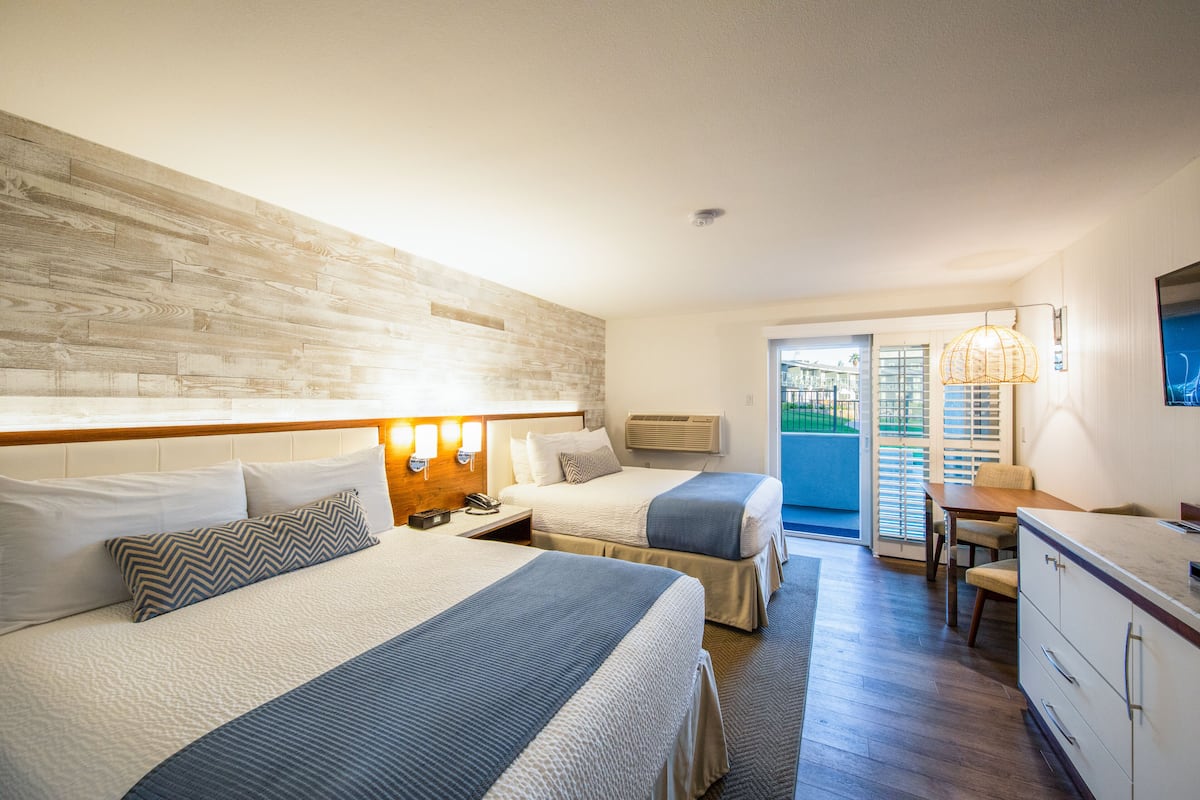 Habitación de hotel con dos camas, un escritorio y vistas al exterior.