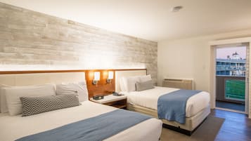 A hotel room with two beds, a wooden headboard, a nightstand with a phone, and a view of a building through a glass door.