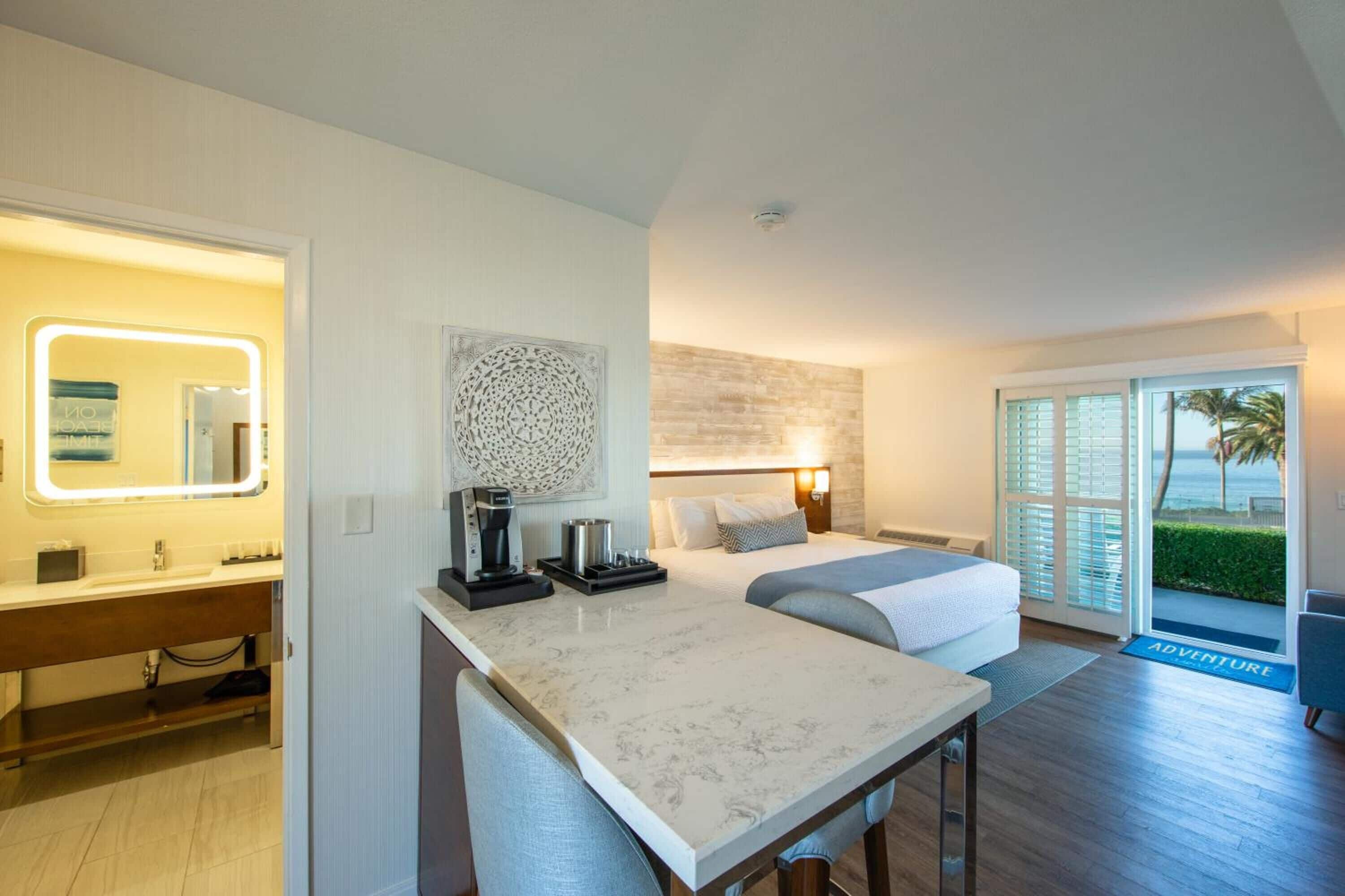 Quarto de hotel moderno com banheiro, área de refeições e cama com vista para o oceano.