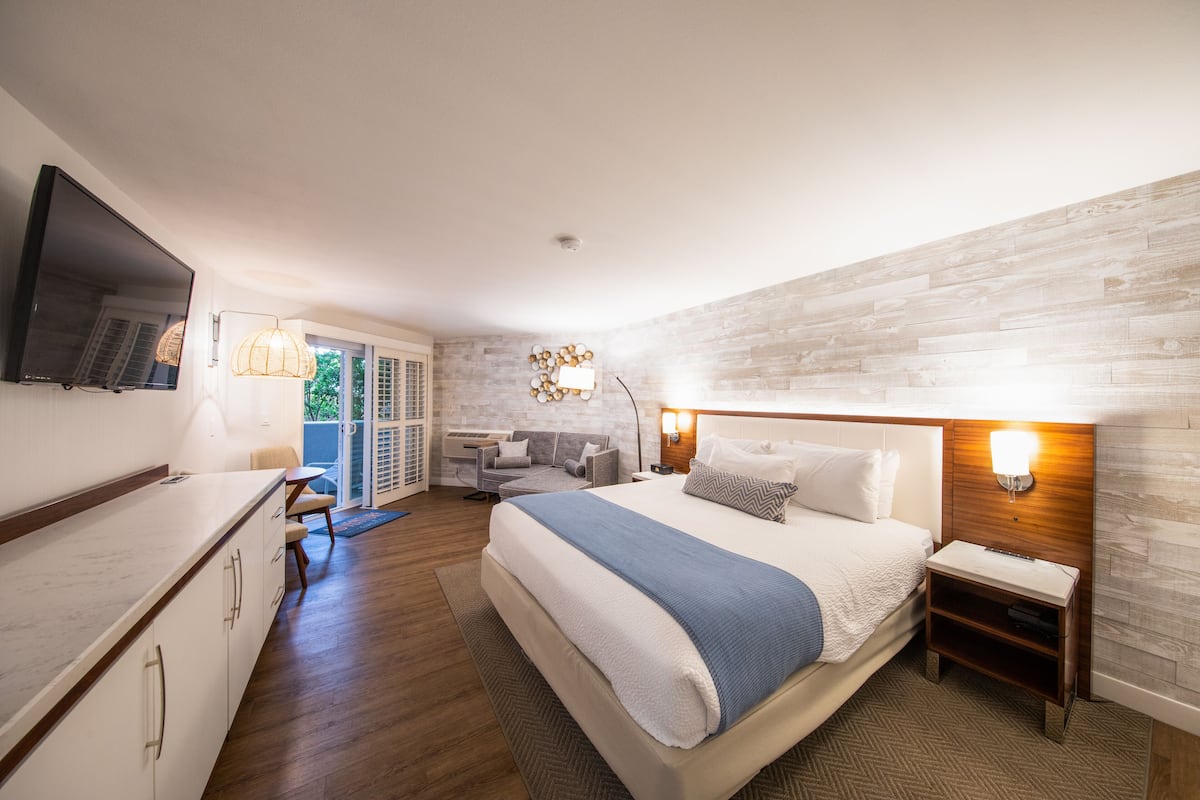 Una habitación de hotel moderna con una cama grande, televisor de pantalla plana, zona de comedor y balcón con vistas.