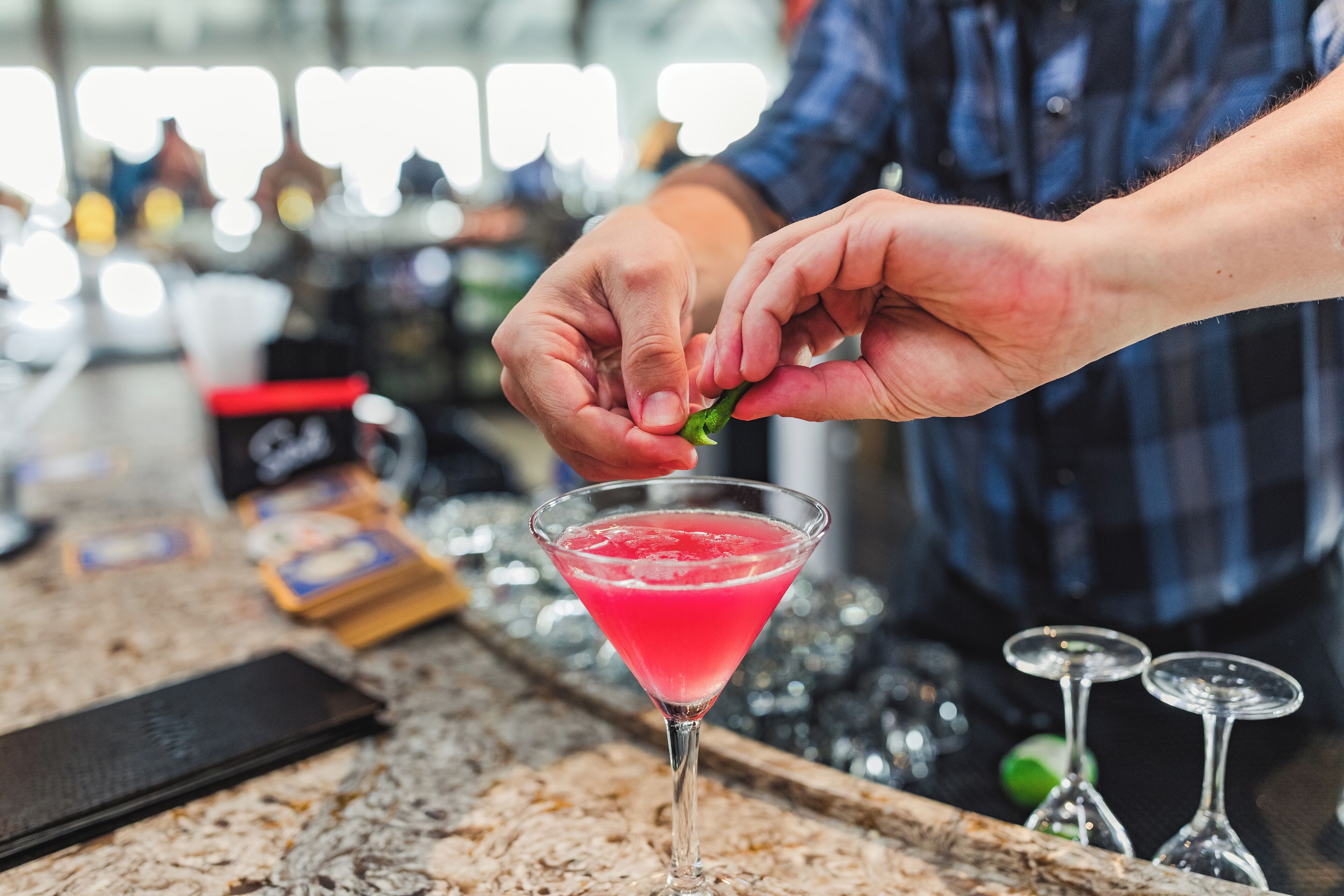 Eine Person dekoriert einen rosa Cocktail mit einer grünen Chilischote.