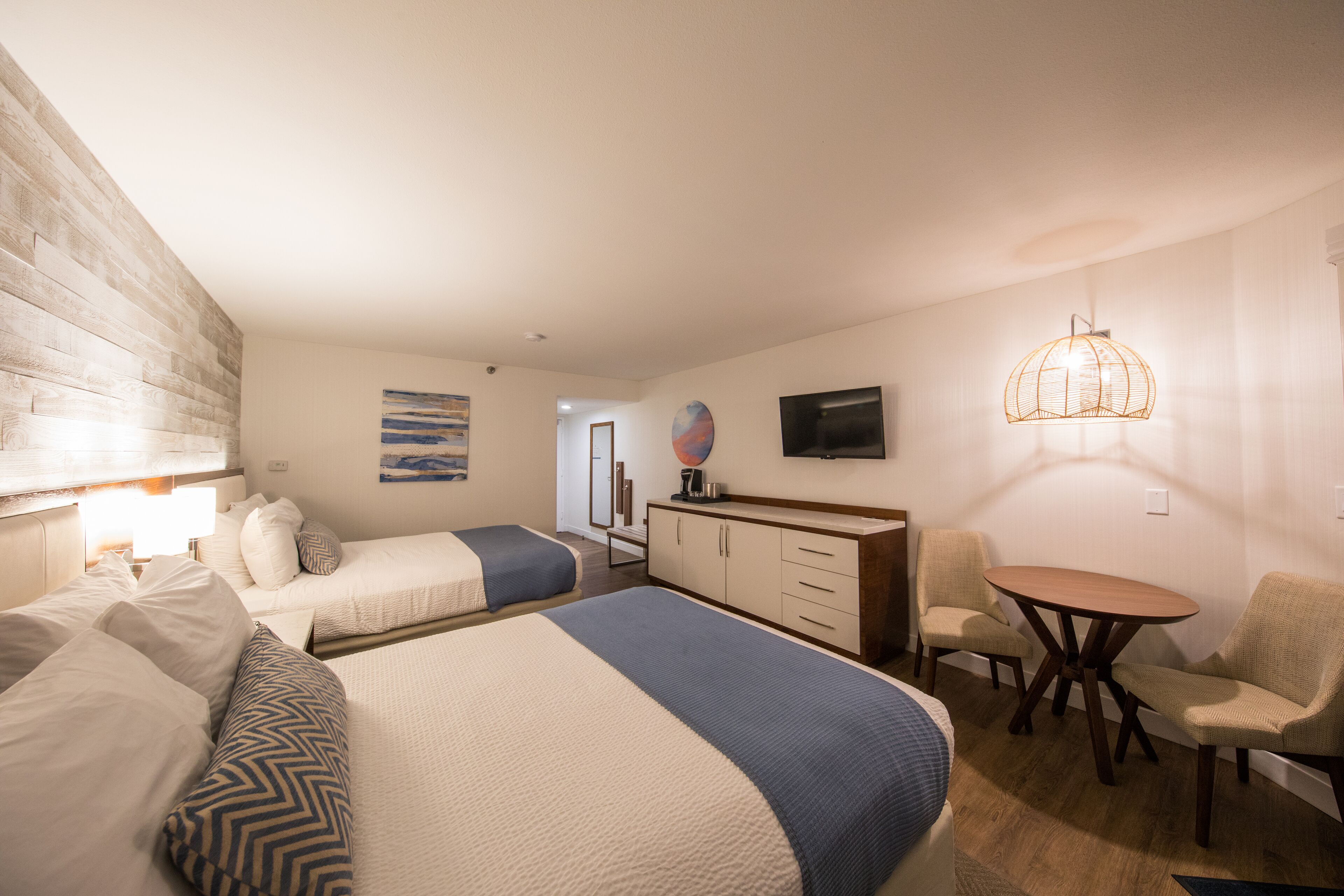 A hotel room with two beds, a desk, a chair, a television, and a hanging light fixture.
