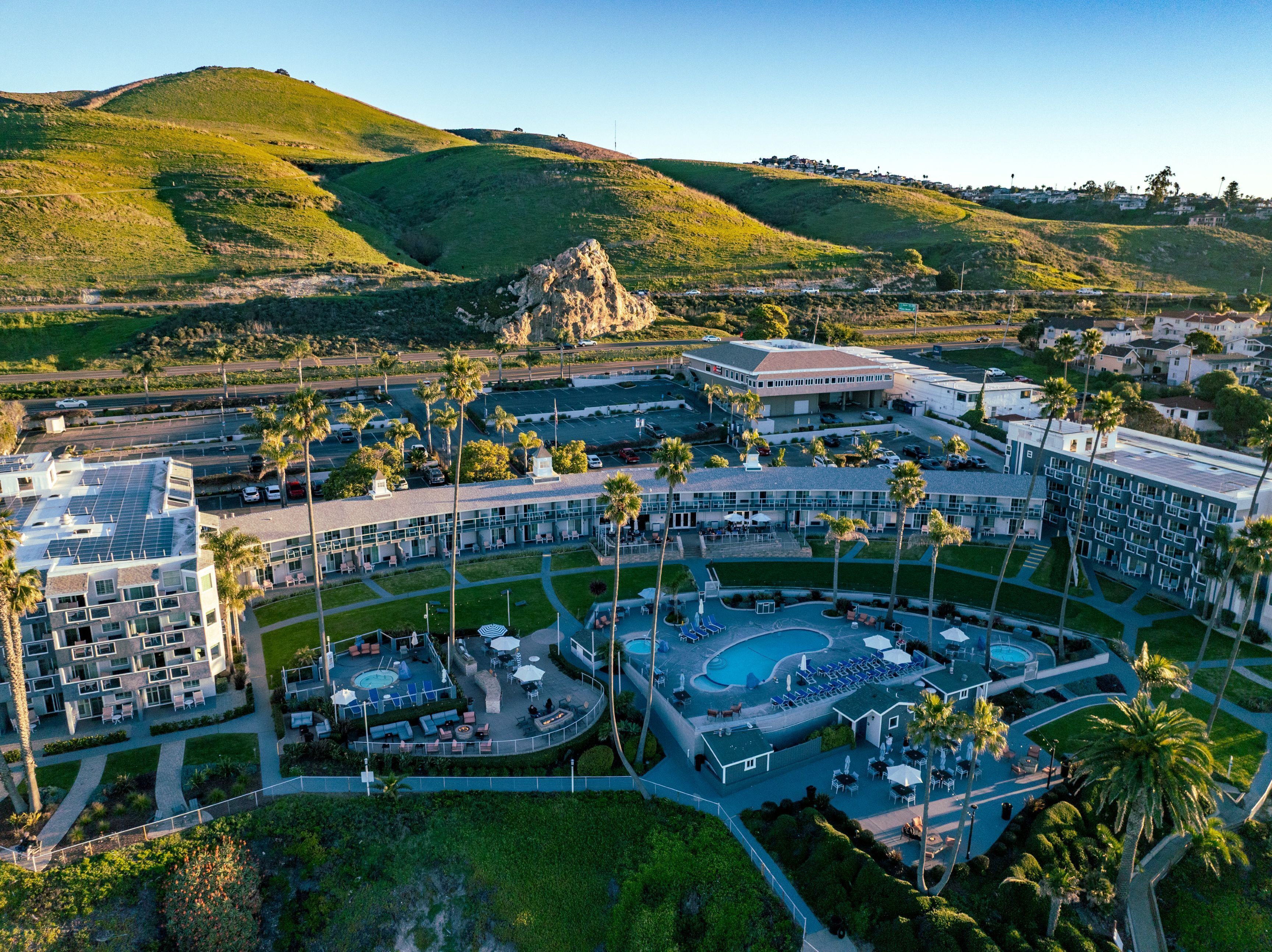 Vista aérea de un resort con piscina, varios edificios y palmeras.