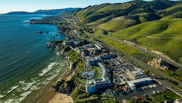 An aerial view of a coastal town with a beach, a marina, and a road leading to the town.