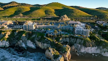 A coastal resort with multiple buildings, a rocky shoreline, and a hilly backdrop.
