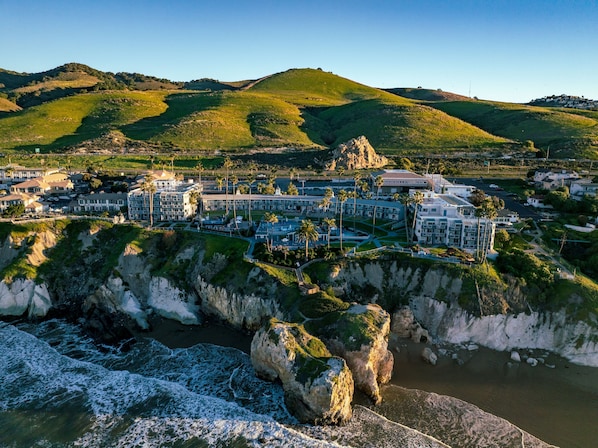A coastal resort with multiple buildings, a rocky shoreline, and a hilly backdrop.