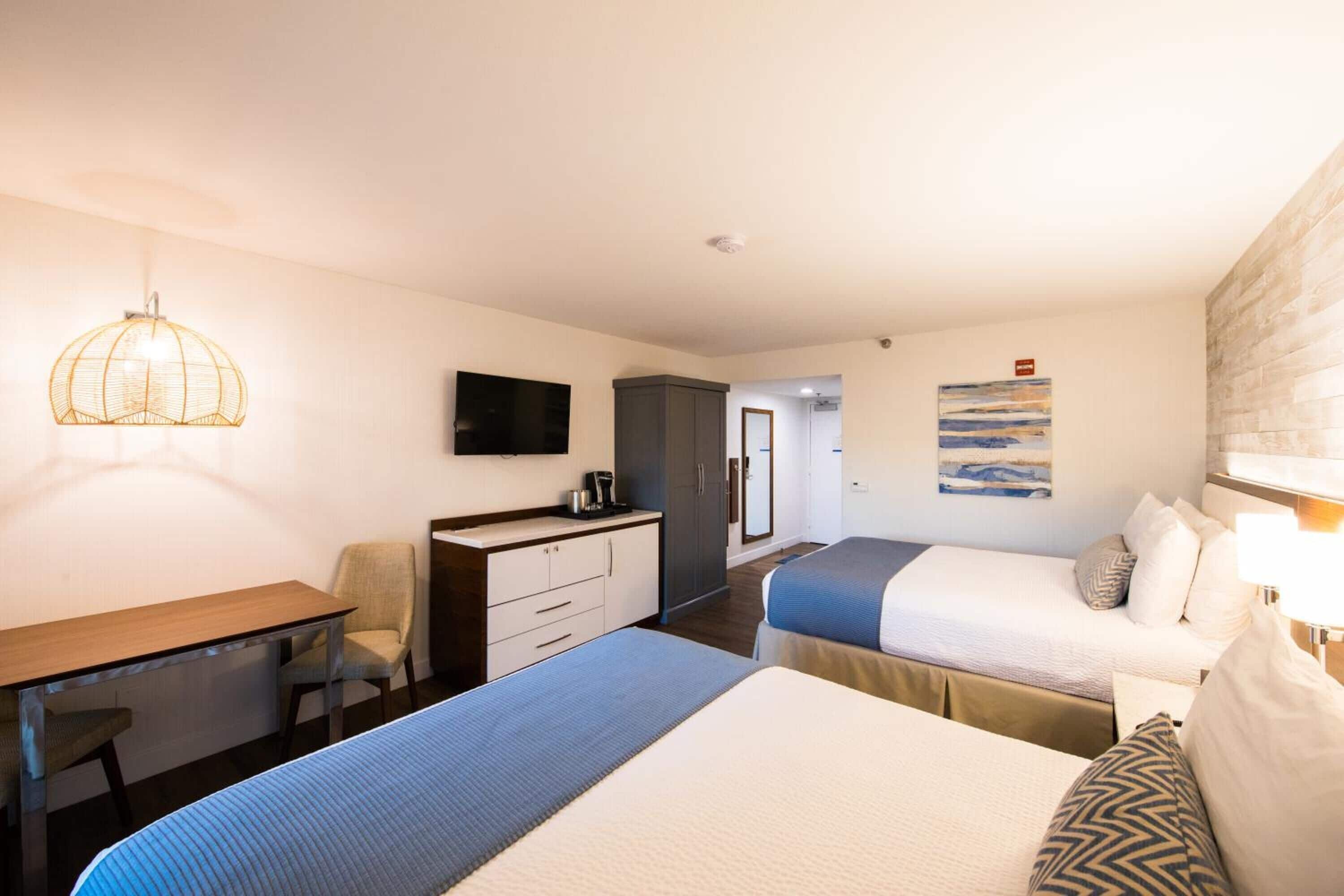 A hotel room with a desk, two beds, a television, and a painting on the wall.