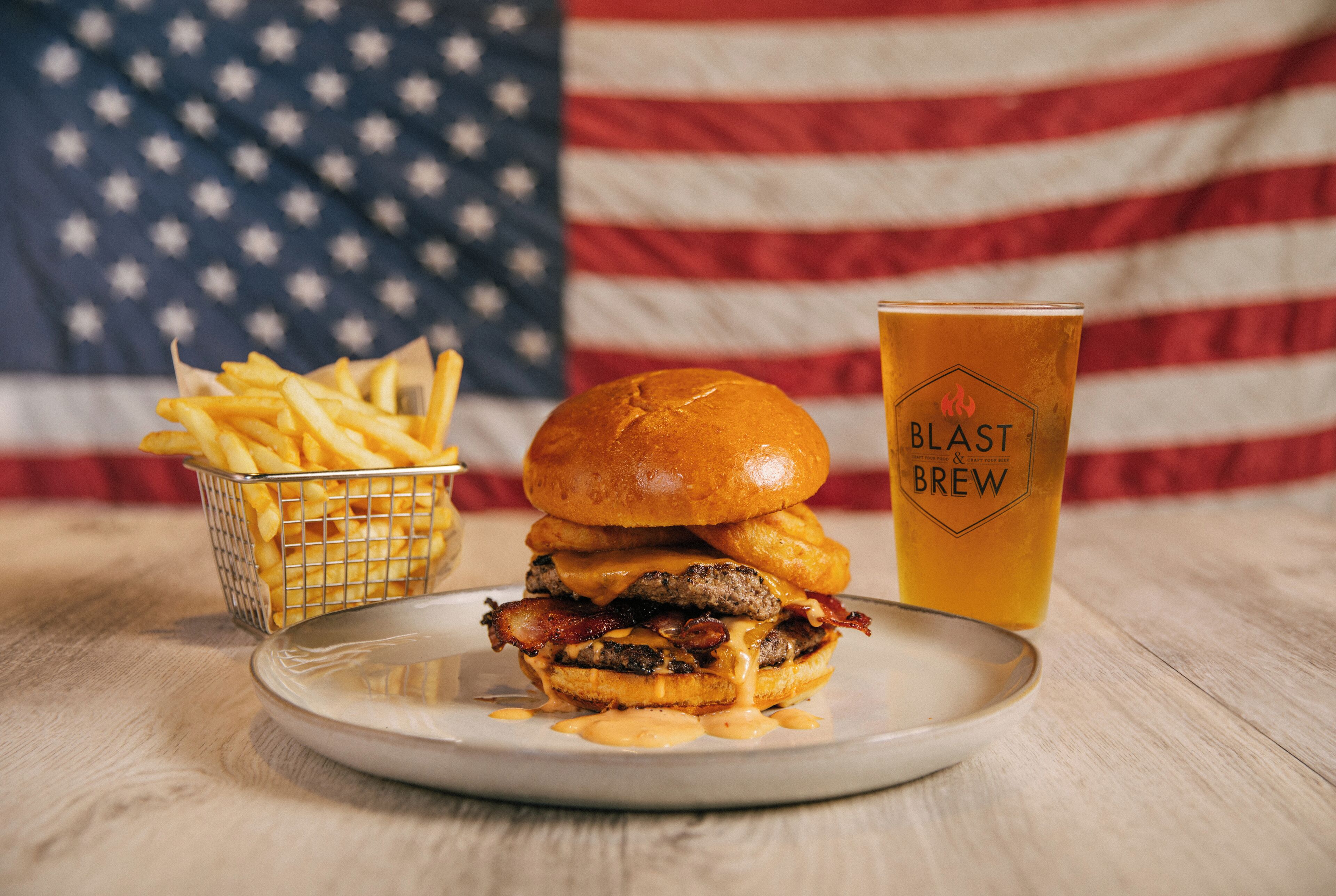 Un hamburger avec du bacon, des frites et un verre de bière, le tout servi sur une assiette avec un drapeau américain en arrière-plan.