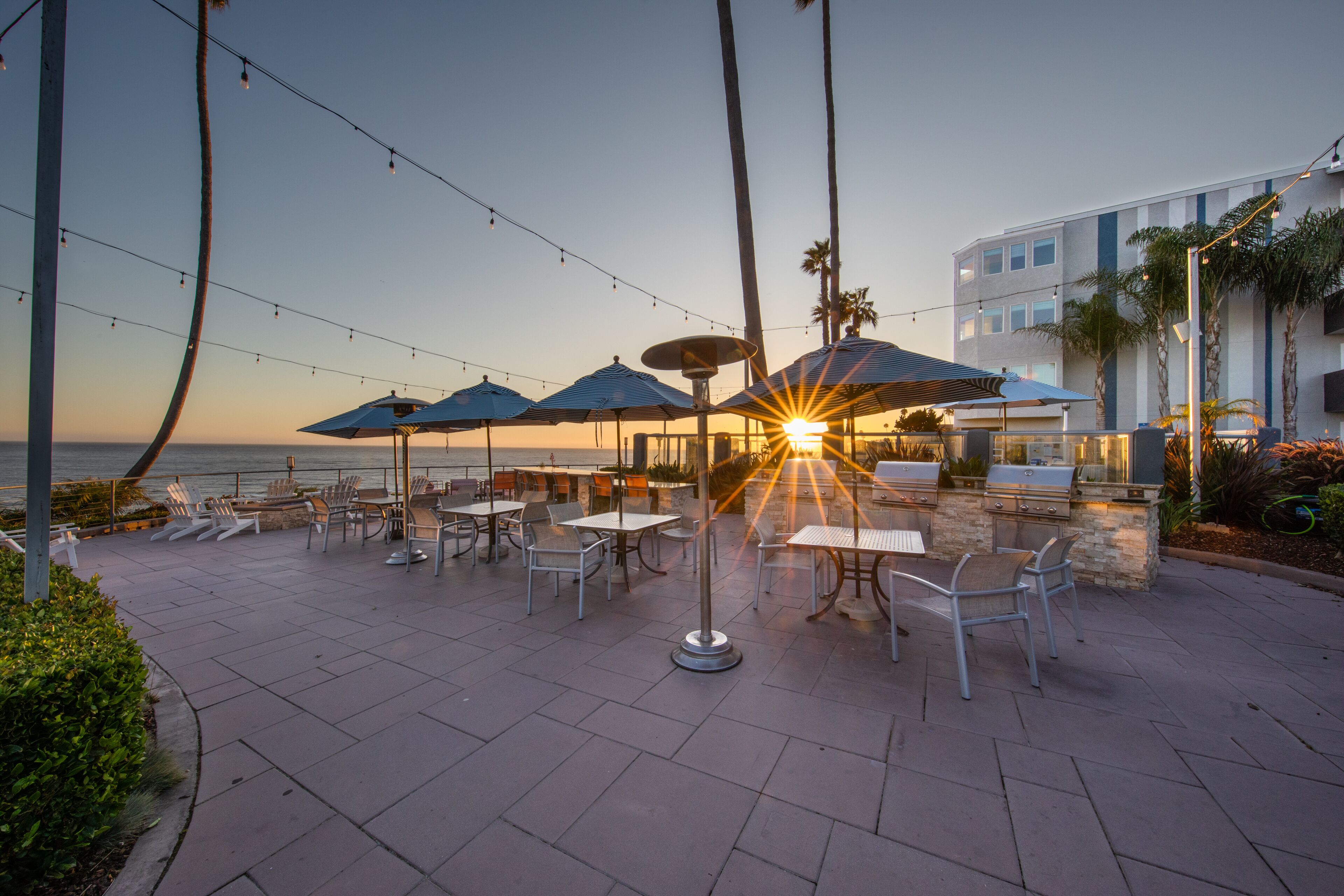 An outdoor patio with tables and chairs, string lights, and umbrellas.