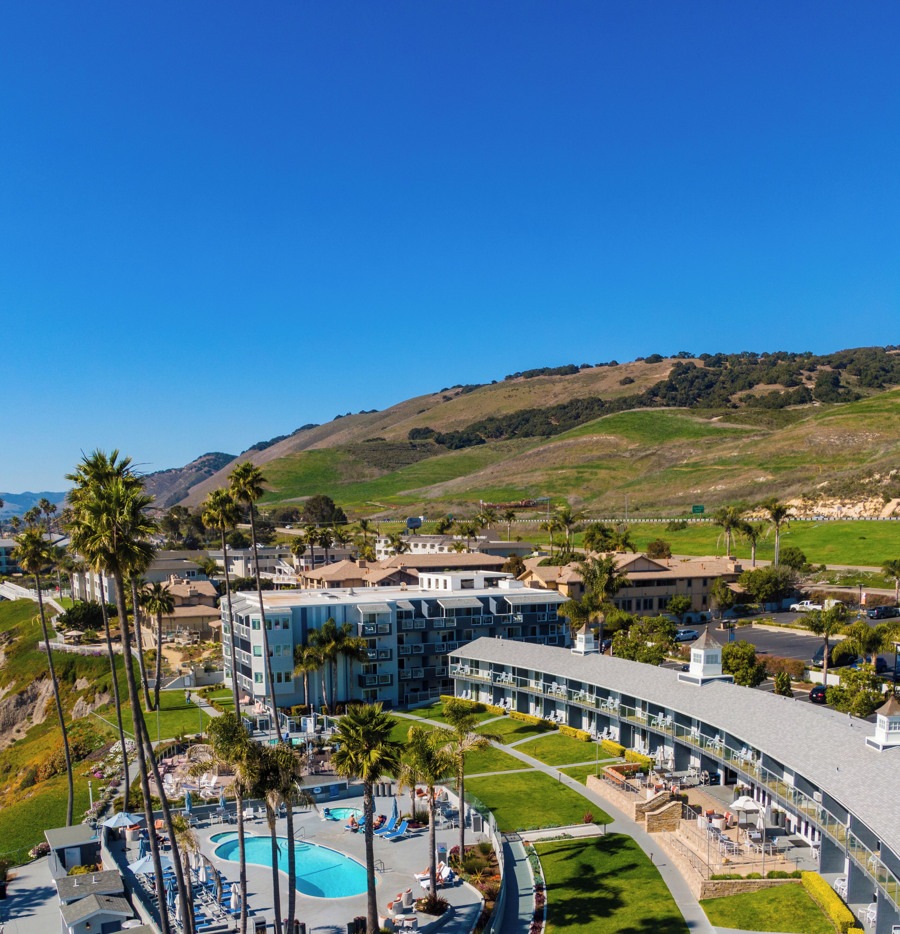 Un complexe hôtelier doté d’une piscine, de palmiers et offrant une vue sur les collines.