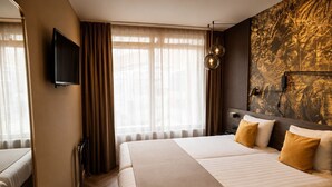A hotel room with a large bed, a television, and a mural on the wall.