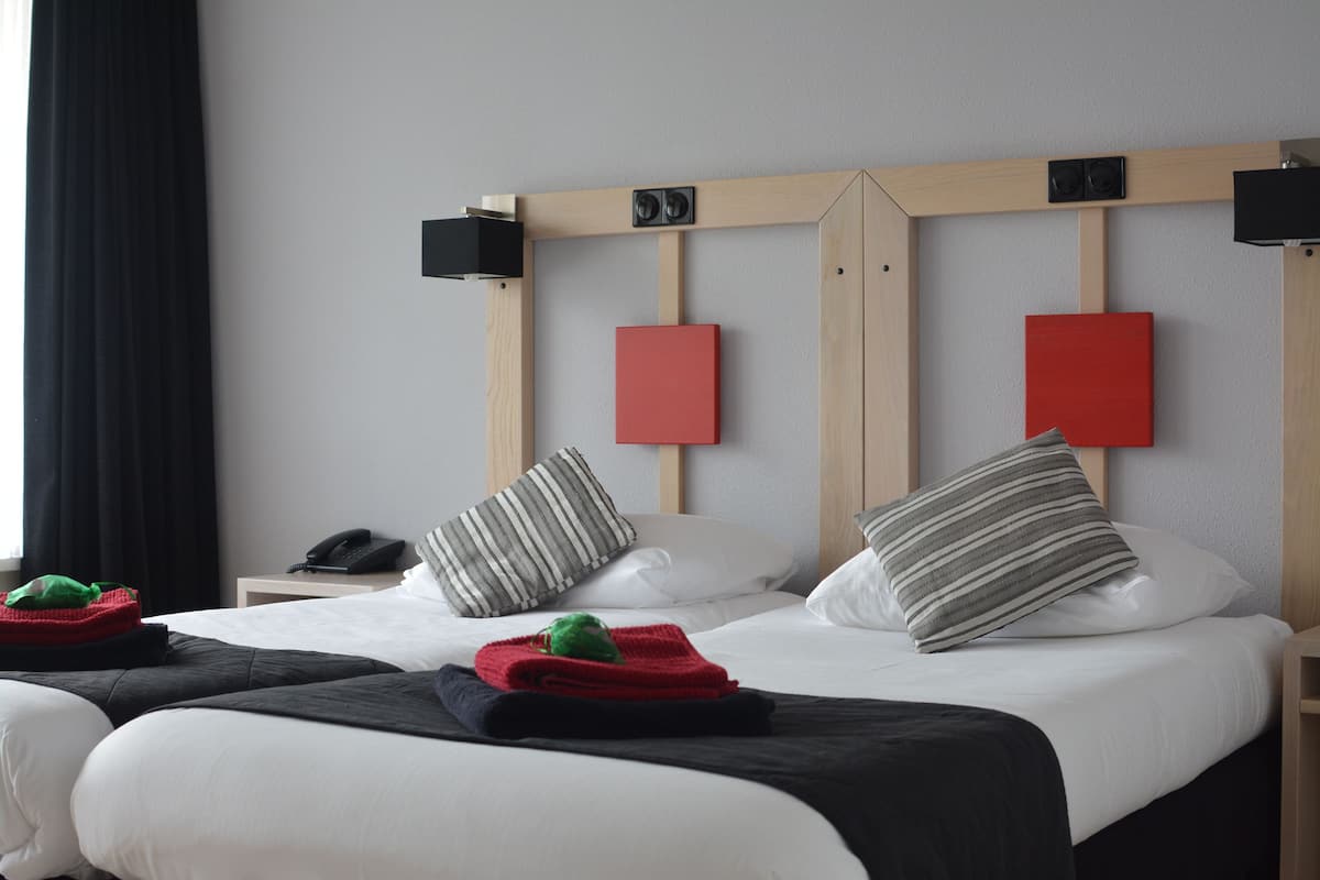 A hotel room with a large bed, two bedside tables, a telephone, and a headboard with speakers.
