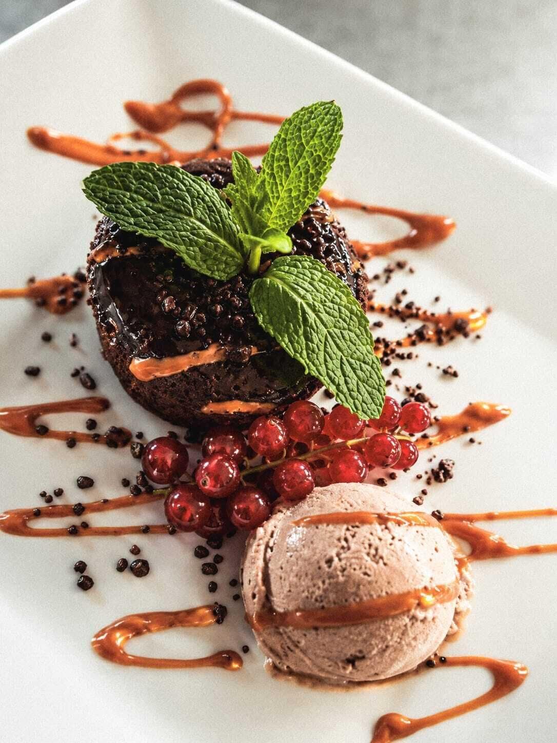 A dessert plate with a chocolate lava cake, red currants, and a scoop of ice cream.